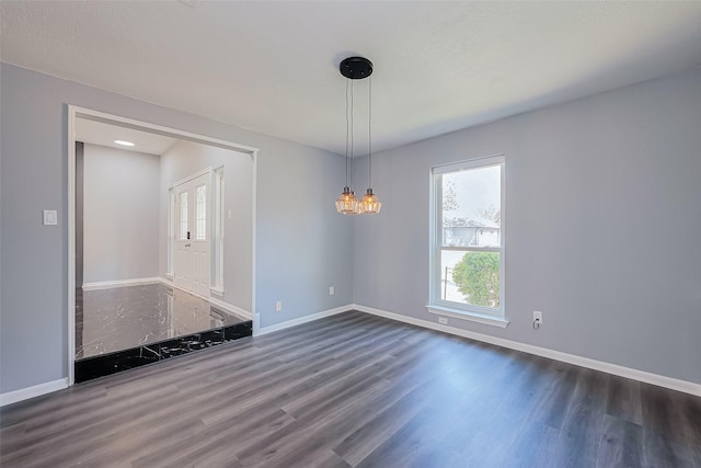 empty room with baseboards, a notable chandelier, and wood finished floors