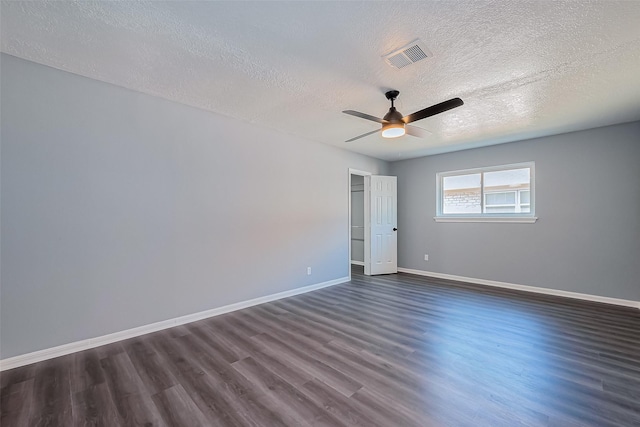 empty room with dark wood-style floors, visible vents, a ceiling fan, and baseboards