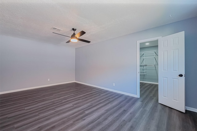 empty room featuring a ceiling fan, visible vents, dark wood-style flooring, and baseboards