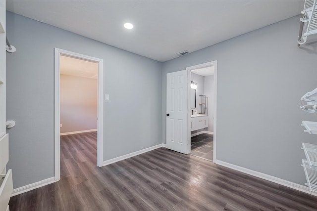 unfurnished bedroom with dark wood-style floors, visible vents, ensuite bathroom, and baseboards