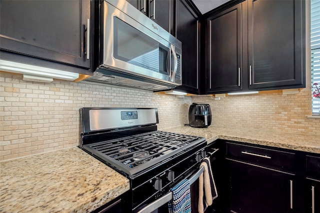 kitchen featuring light stone counters, stainless steel appliances, tasteful backsplash, and dark cabinetry