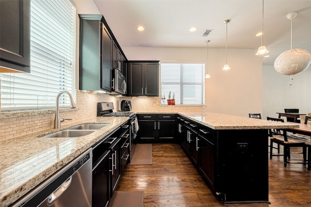 kitchen featuring light stone countertops, decorative backsplash, appliances with stainless steel finishes, dark wood-style floors, and a sink