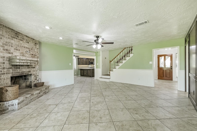 unfurnished living room with visible vents, a fireplace, wainscoting, and stairway