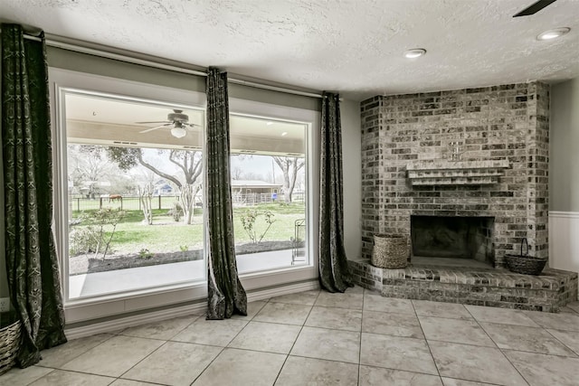 unfurnished living room featuring light tile patterned floors, a ceiling fan, a fireplace, and a textured ceiling