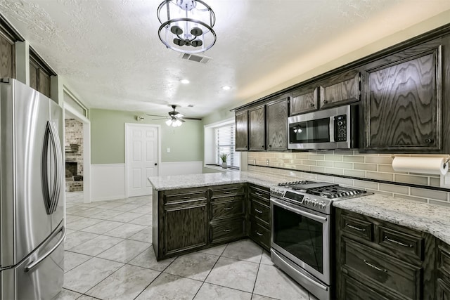 kitchen featuring visible vents, wainscoting, appliances with stainless steel finishes, a textured ceiling, and a ceiling fan