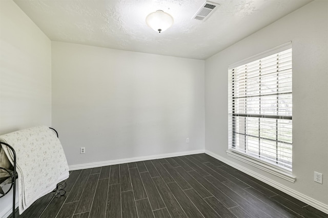 unfurnished room featuring baseboards, visible vents, dark wood-style flooring, and a textured ceiling