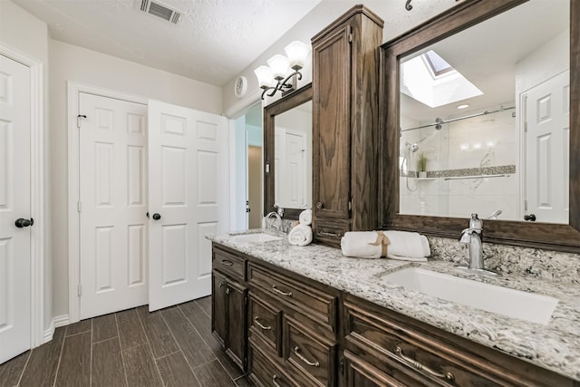 bathroom featuring visible vents, a stall shower, a skylight, and a sink