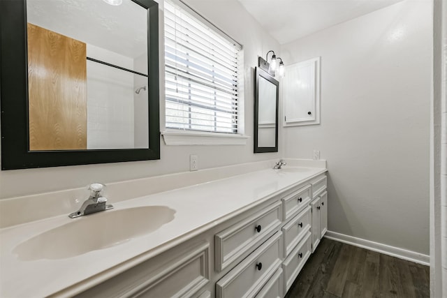 full bath featuring double vanity, wood finished floors, baseboards, and a sink