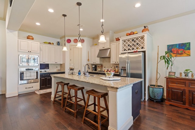 kitchen featuring a kitchen bar, dark wood-type flooring, under cabinet range hood, a sink, and stainless steel appliances