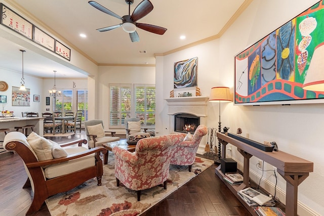 living room with ornamental molding, ceiling fan with notable chandelier, hardwood / wood-style floors, recessed lighting, and a lit fireplace