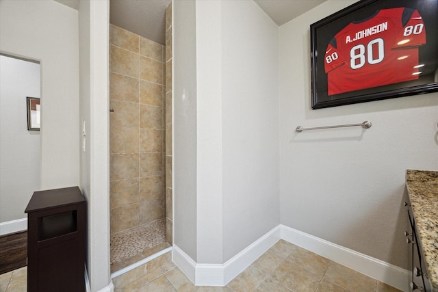 bathroom featuring tile patterned floors, baseboards, tiled shower, and vanity