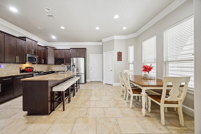 kitchen featuring visible vents, a sink, a kitchen breakfast bar, appliances with stainless steel finishes, and decorative backsplash