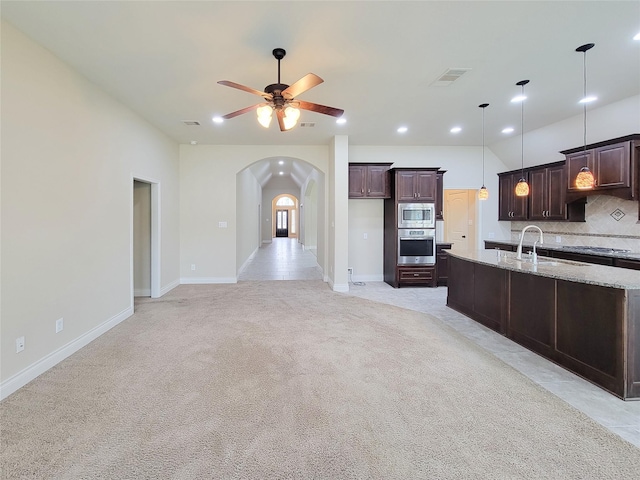 kitchen featuring a ceiling fan, stainless steel appliances, arched walkways, decorative backsplash, and light colored carpet