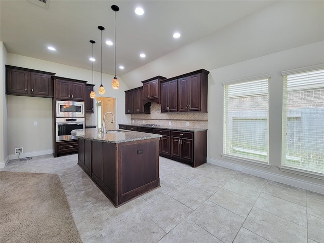 kitchen with a center island with sink, stone countertops, a sink, decorative backsplash, and appliances with stainless steel finishes