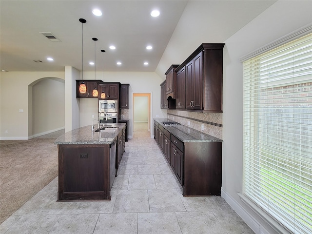 kitchen featuring dark brown cabinets, backsplash, dark stone counters, appliances with stainless steel finishes, and arched walkways