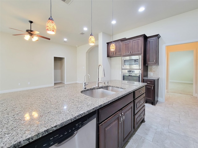 kitchen with ceiling fan, light stone counters, arched walkways, stainless steel appliances, and a sink