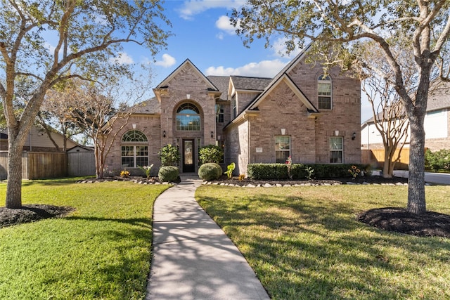 view of front of home with brick siding, roof with shingles, a front yard, and fence