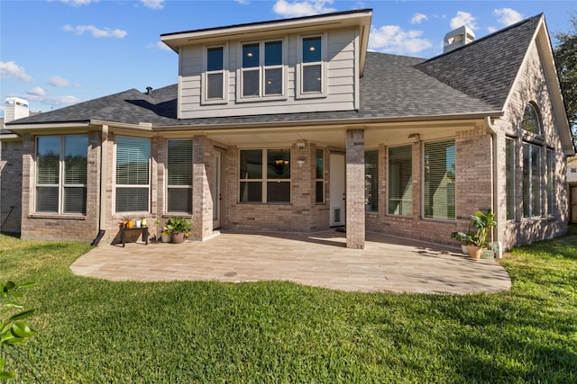 back of property featuring brick siding, a lawn, a shingled roof, and a patio