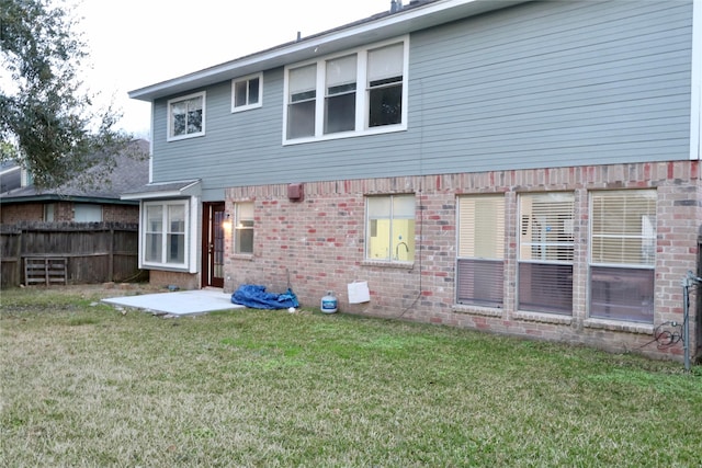 rear view of property with a patio area, a lawn, brick siding, and fence