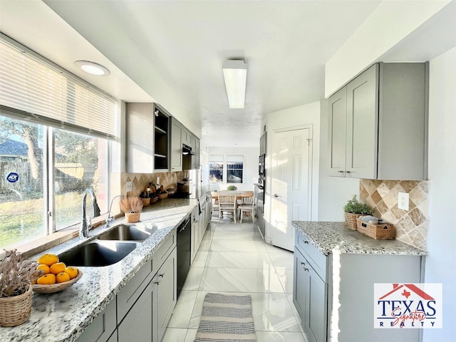 kitchen featuring gray cabinetry, light stone countertops, dishwasher, and a sink