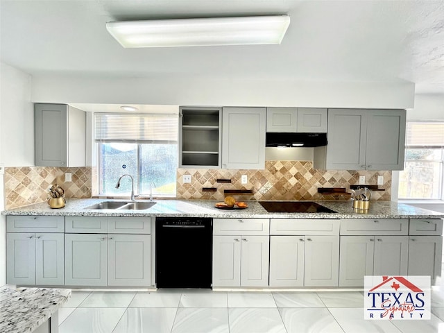 kitchen featuring under cabinet range hood, light stone counters, gray cabinets, black appliances, and a sink