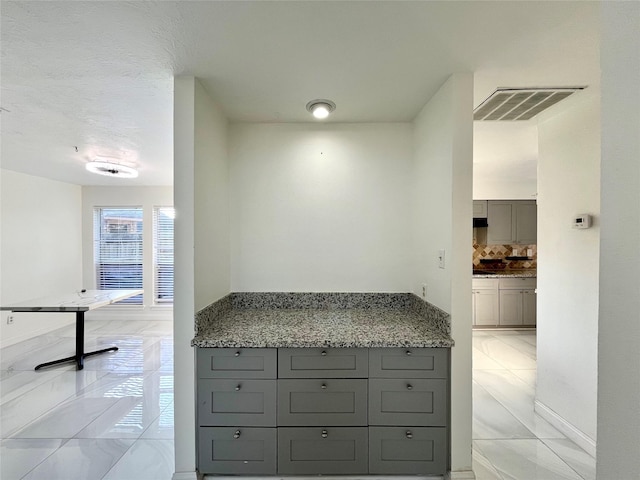 kitchen featuring backsplash, visible vents, gray cabinets, and light stone counters