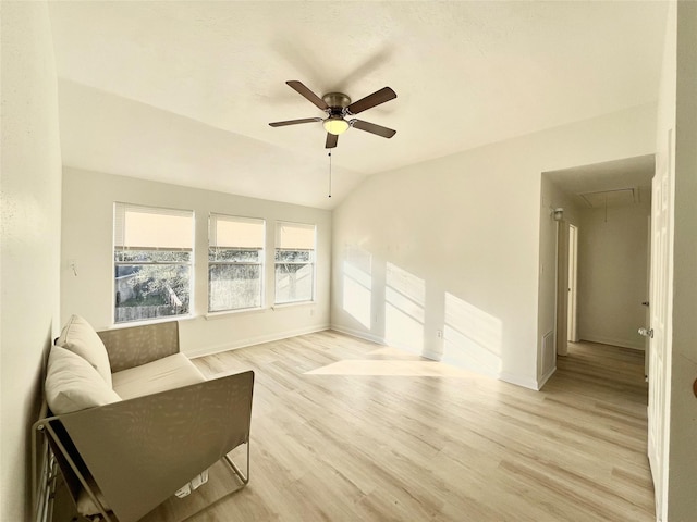 living area featuring a ceiling fan, light wood finished floors, baseboards, attic access, and vaulted ceiling