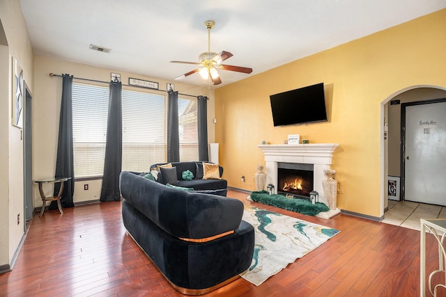 living room with visible vents, a warm lit fireplace, hardwood / wood-style floors, arched walkways, and ceiling fan