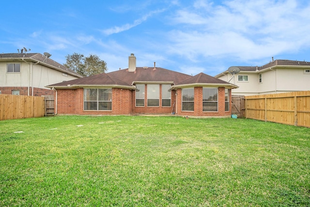 rear view of property featuring a lawn, brick siding, a fenced backyard, and a chimney