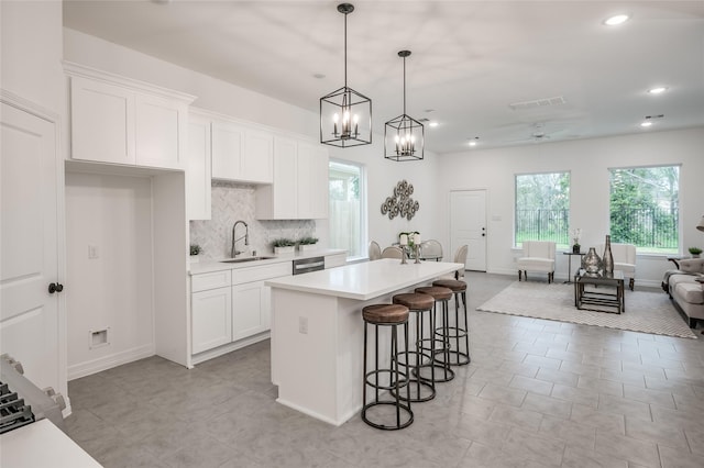 kitchen featuring a center island with sink, a sink, light countertops, white cabinetry, and a kitchen bar