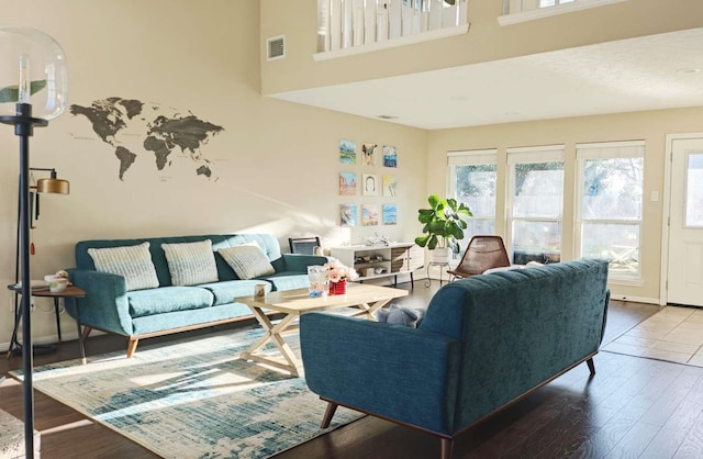 living area featuring wood finished floors, visible vents, a towering ceiling, and baseboards