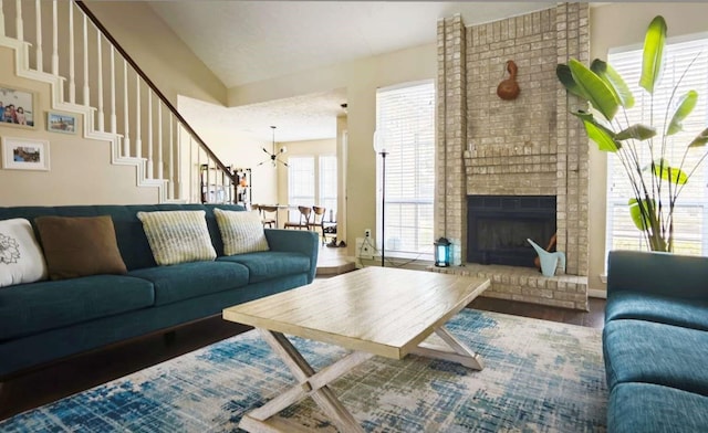 living area with stairs, vaulted ceiling, a fireplace, an inviting chandelier, and wood finished floors