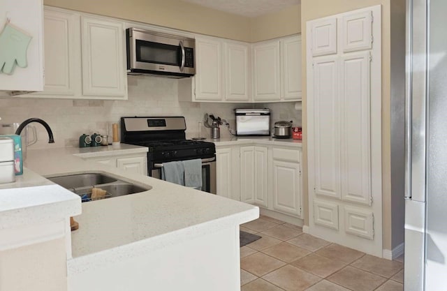 kitchen featuring light tile patterned flooring, a sink, appliances with stainless steel finishes, white cabinetry, and backsplash