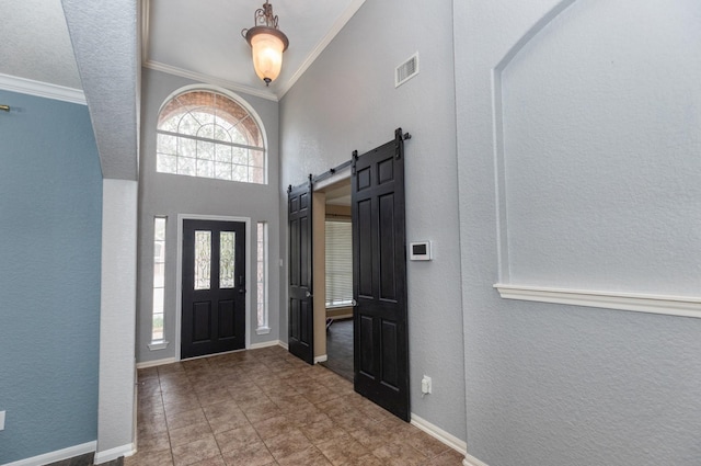 foyer featuring a barn door, baseboards, visible vents, and ornamental molding