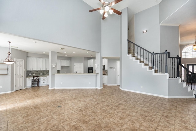 unfurnished living room featuring ceiling fan, stairs, and baseboards
