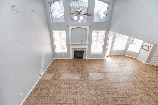 unfurnished living room featuring visible vents, a high ceiling, a fireplace, baseboards, and ceiling fan