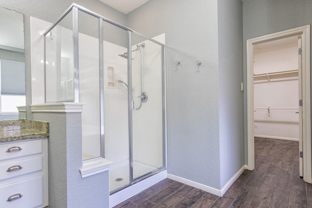 full bathroom with baseboards, a spacious closet, wood finished floors, and a shower stall