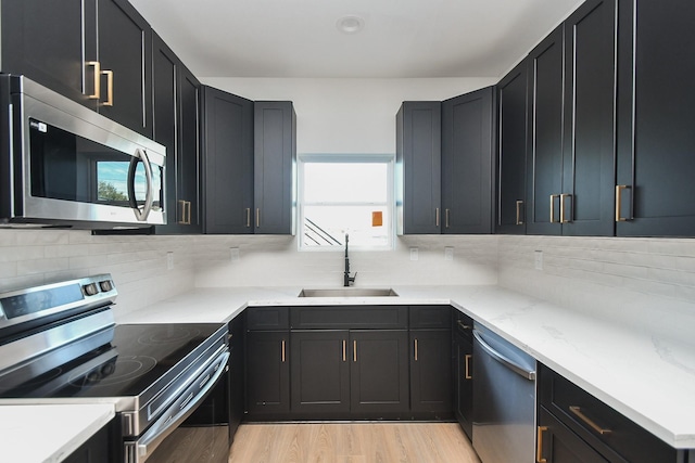 kitchen featuring dark cabinetry, light stone countertops, a sink, stainless steel appliances, and tasteful backsplash