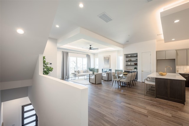 living room with a raised ceiling, recessed lighting, wood finished floors, and visible vents