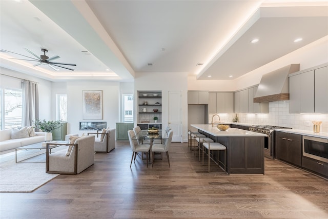 kitchen featuring open floor plan, a kitchen bar, custom range hood, wood finished floors, and stainless steel appliances