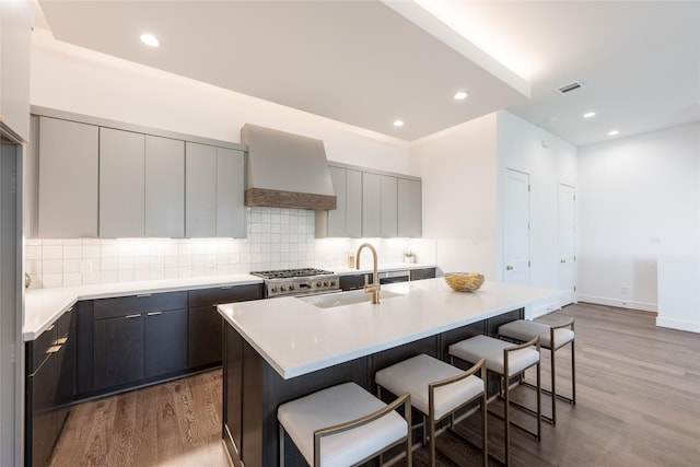 kitchen with a center island with sink, custom range hood, a sink, a kitchen breakfast bar, and wood finished floors