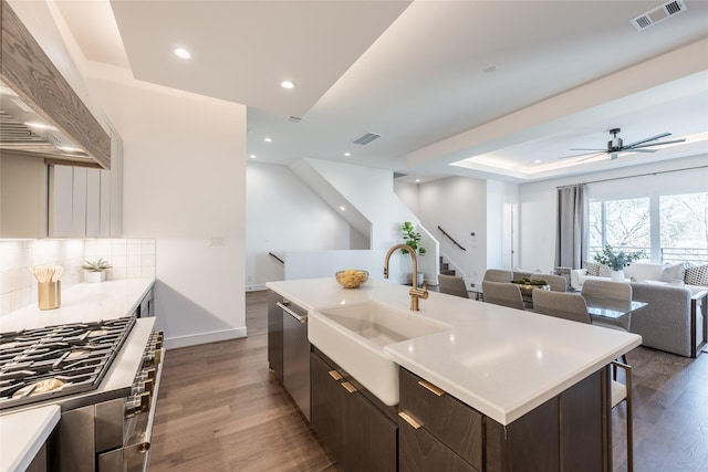 kitchen featuring visible vents, a sink, dark brown cabinetry, custom range hood, and dishwasher