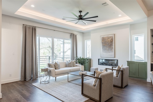 living room featuring a tray ceiling, wood finished floors, visible vents, and ceiling fan