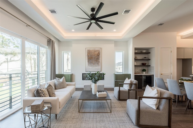 living area featuring visible vents, wood finished floors, a raised ceiling, and ceiling fan