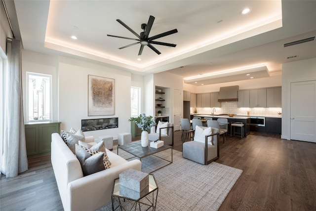 living area with dark wood finished floors, visible vents, a ceiling fan, and a tray ceiling