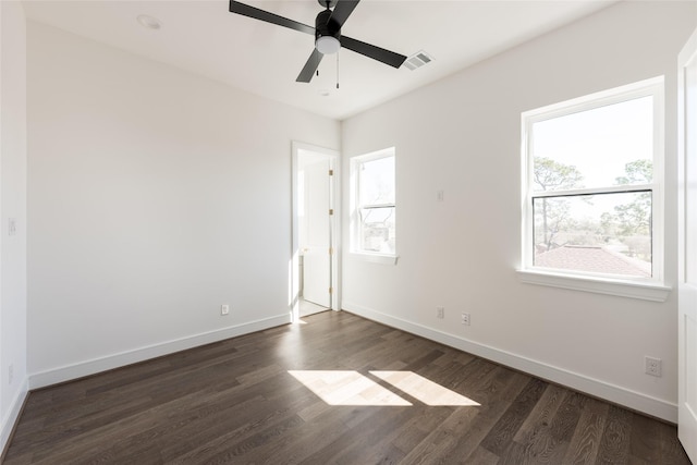 empty room featuring ceiling fan, visible vents, baseboards, and dark wood finished floors