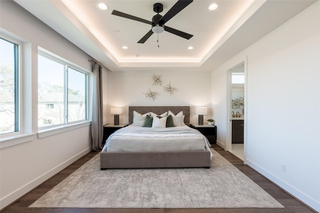 bedroom with a raised ceiling, dark wood finished floors, recessed lighting, connected bathroom, and baseboards