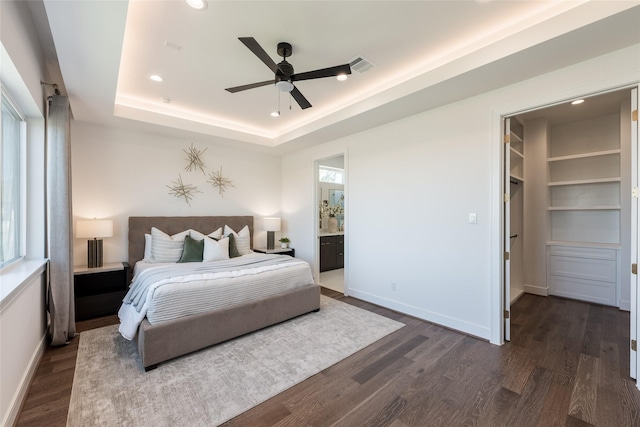 bedroom featuring baseboards, visible vents, dark wood finished floors, a tray ceiling, and a walk in closet