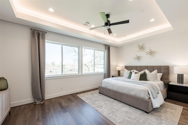 bedroom with visible vents, baseboards, a tray ceiling, recessed lighting, and dark wood-style floors