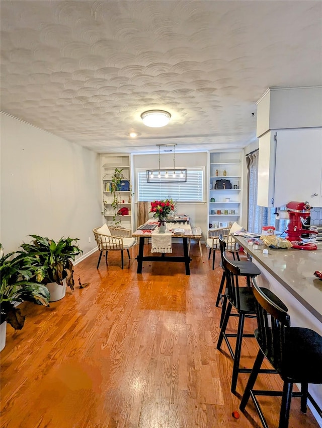 dining area with built in features, light wood-style floors, and a textured ceiling